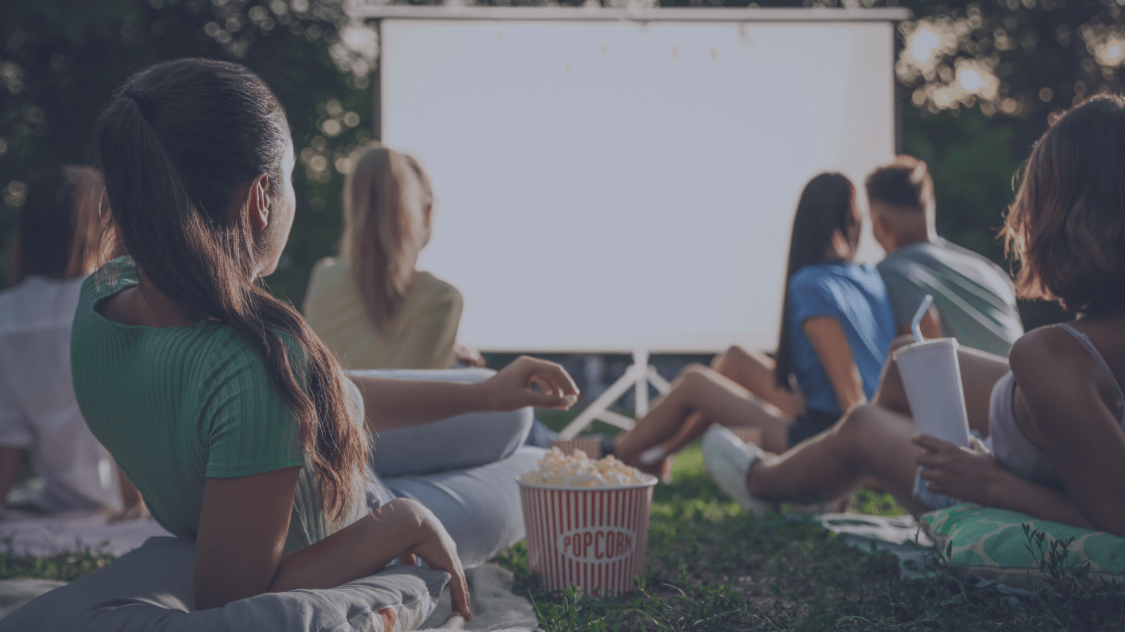 People sitting on the grass eating popcorn, waiting for the outdoor movie to start.