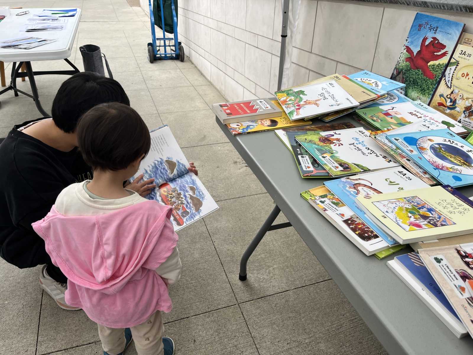 A mom with her child reading a book in front of the literacy Burnaby now table, which is full of books at one of the events