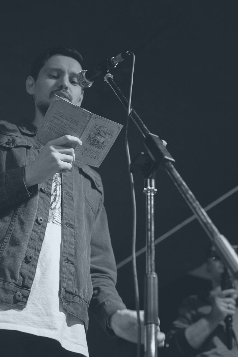 black and white photo of a man reading poetry book in front of a microphone