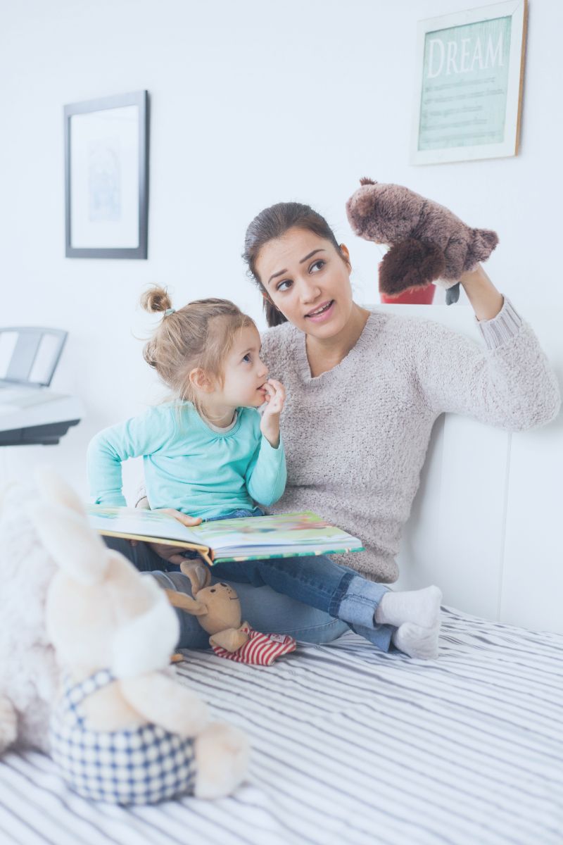A mom telling her child a story with puppets and a children's book.