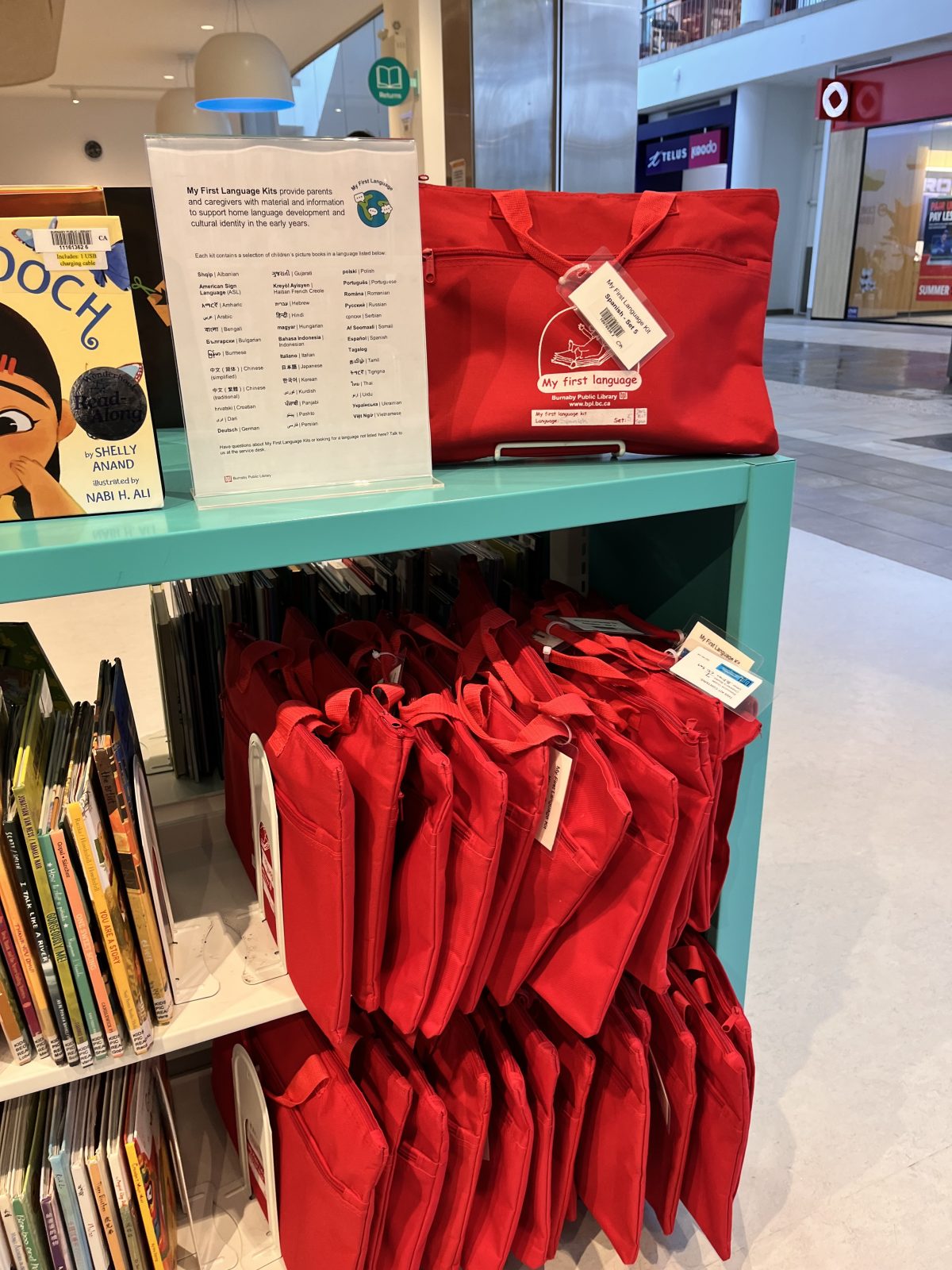 A list of the languages offered next to a red bag with My First Language Kit for Spanish on top of a turquoise shelf, on the bottom more My First Language Kit red bags.